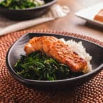 Miso salmon on a bed of white rice and steamed spinach in a black bowl.