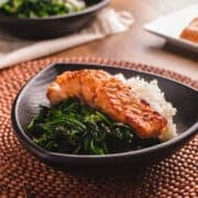 Miso salmon on a bed of white rice and steamed spinach in a black bowl.