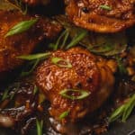 Chicken Adobo in a black pan topped with green onions and black peppercorns.