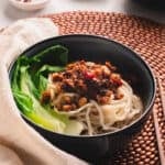 Dan dan noodles in a blue bowl with chopsticks on a wooden beaded placemat.