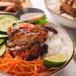 Silver spoon drizzling on nuoc cham sauce over lemongrass chicken rice bowl with cucumbers & carrots.