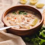 Tom kha soup in a wooden bowl on a white table with a silver spoon.