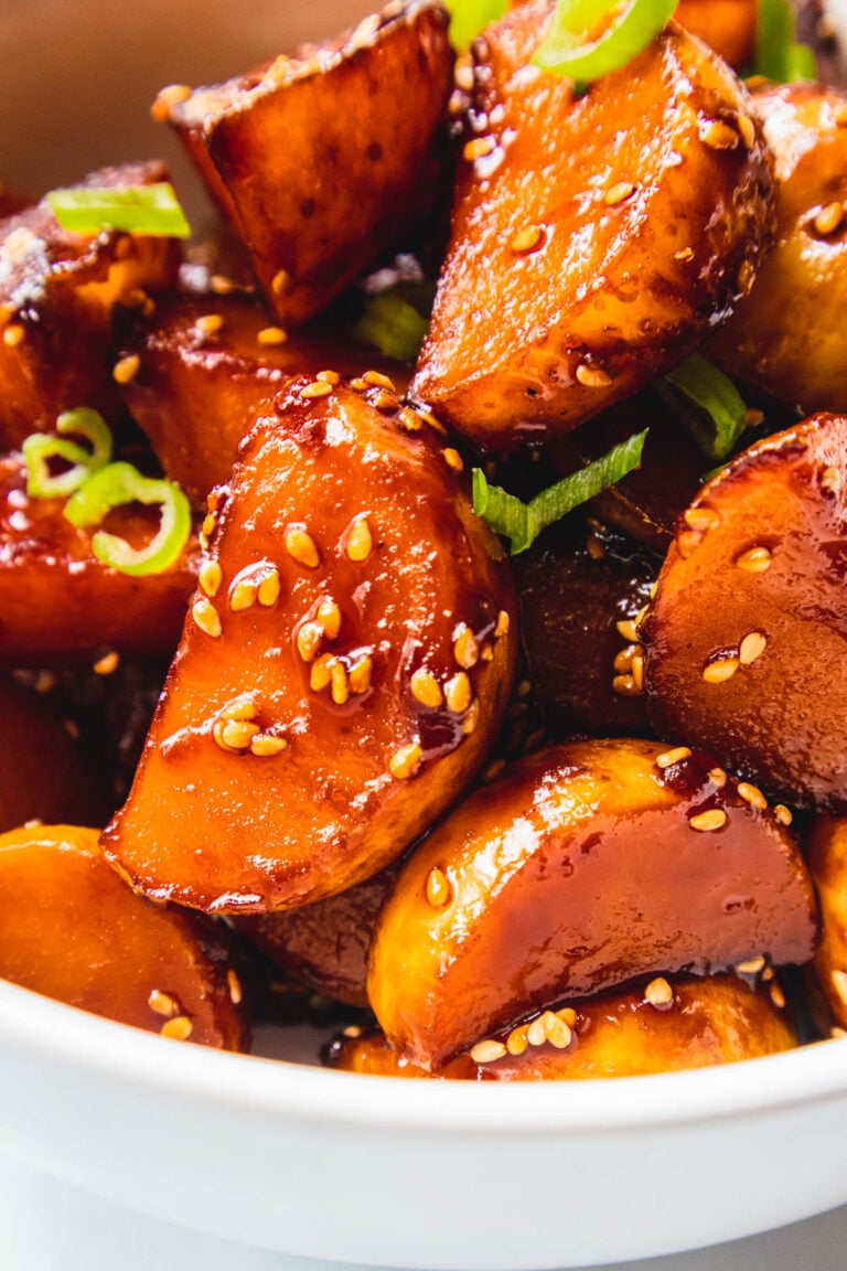 Sticky honey potatoes topped with sesame seeds and green onions in a white bowl.