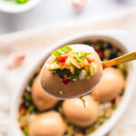 Spoon holding korean marinated egg with aromatics on top.