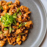 Blue plate of sesame chicken topped with sesame seeds and green onions.