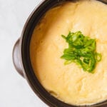 Steamed egg topped with green onions in a black stoneware pot.