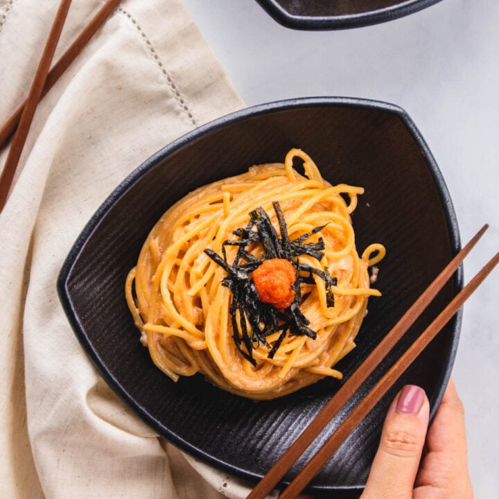 Holding plate of mentaiko pasta with chopsticks.