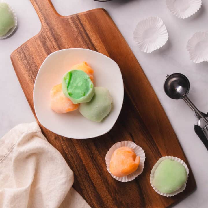 Green and orange mochi ice cream on a white place.
