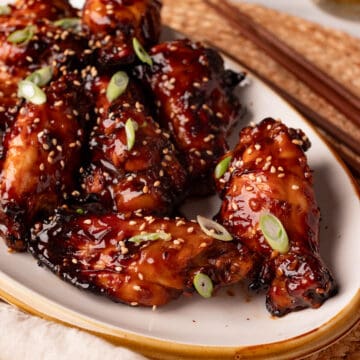 Soy sauce chicken wings on an oval plate with sesame seeds & green onions.