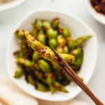 Chopsticks holding a piece of spicy garlic edamame.