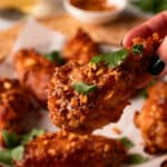 Holding golden brown chicken wings with chopped cilantro and garlic crisps.