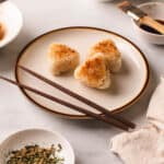 White plate of yaki onigiri with chopsticks on a white table.