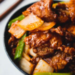 Beef onions stir-fry in a black bowl with wooden chopsticks behind.