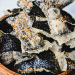 Wooden bowl with seaweed chips on a white table.