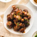 Square plate of miso mushrooms garnished with chopped chives.