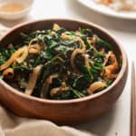 Sauteed spinach with onions in a wooden bowl topped with sesame seeds.