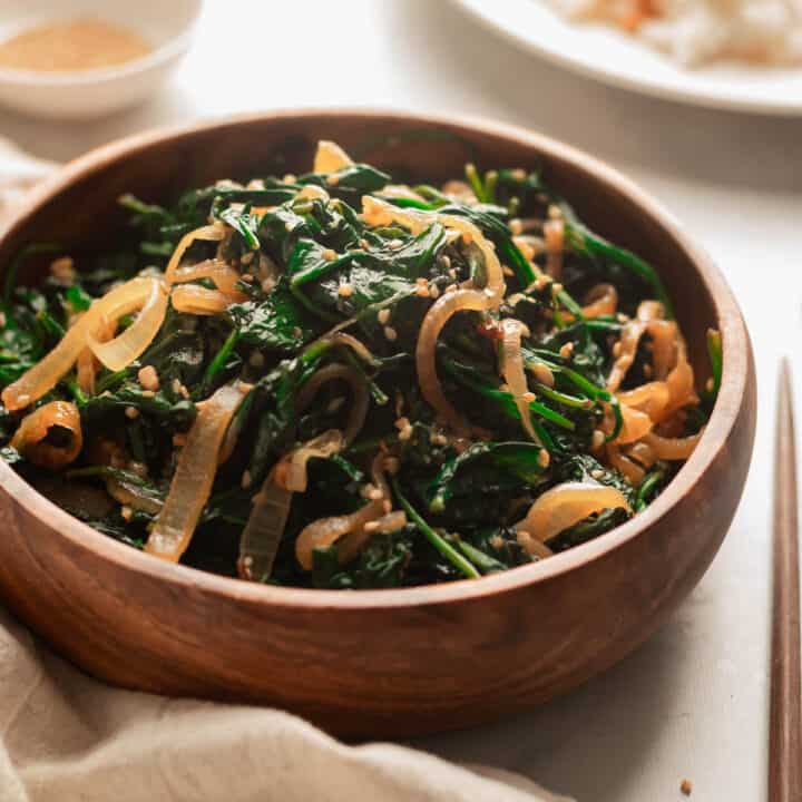 Sauteed spinach with onions in a wooden bowl topped with sesame seeds.