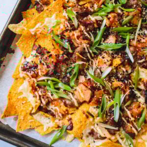Baking tray of bulgogi nachos with cut kimchi pieces on top.