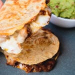 Holding ublgogi quesadilla on a blue plate with a white bowl of guacamole behind.