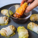 Blue plate of cabbage rolls and dipping cabbage roll in sauce in the center bowl.