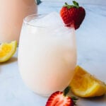 Glass cup and pitcher with strawberry lemonade and topped with fresh strawberries.
