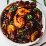 White bowl with pad see ew with shrimp and veggies and chilies behind.