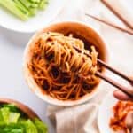 Chopsticks lifting bibim guksu noodles from bowl.