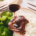 Silver spoon drizzling teriyaki sauce on rice plate of chicken and broccoli.