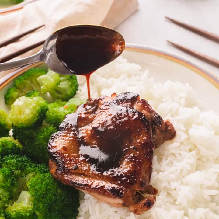 Silver spoon drizzling teriyaki sauce on rice plate of chicken and broccoli.