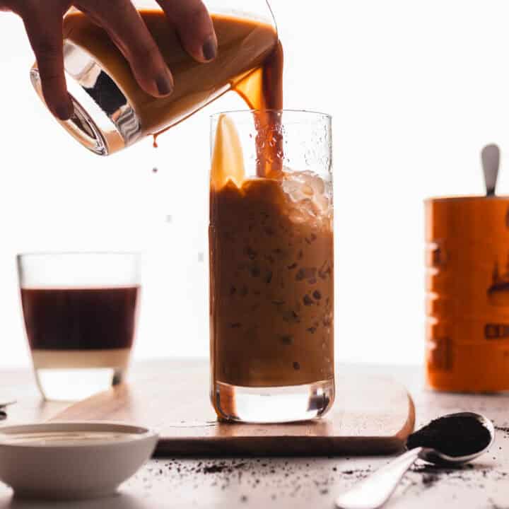 Pouring Vietnamese coffee into a tall glass of ice.