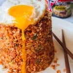Ramen fried rice on a white plate with a fried egg on top and wooden chopsticks.
