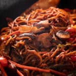 Wok of vegetable lo mein stirred with a wooden spoon.