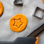 Parament-lined baking sheet with star stamped dalgona with triangle and square metal cookie cutters.