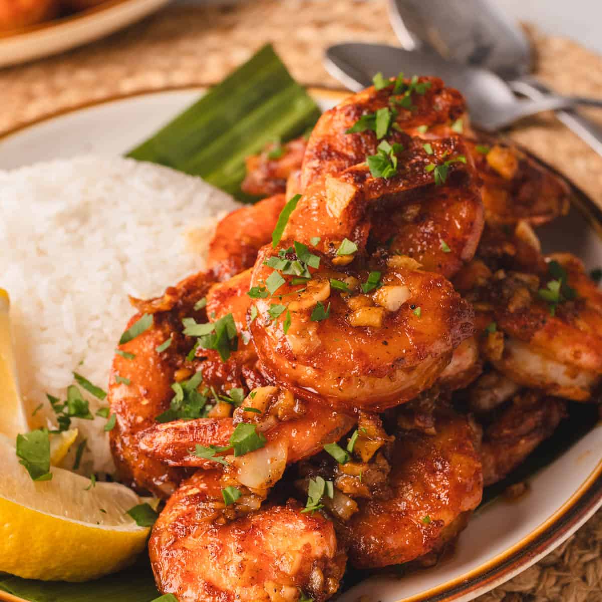 Hawaiian garlic shrimp with rice and lemon wedges on a white plate.