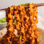 Lifting spicy garlic noodles from square bowl using chopsticks.
