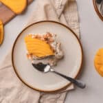 Slice of mango float on a white & browned rimmed plate with a silver spoon.