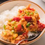 White bowl and silver spoon with rice and tomato egg stir-fry topped with green onions.