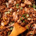Wooden spoon scooping chicken fried rice in a wok.