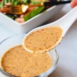 White spoonful goma sesame dressing with a green salad in the back.