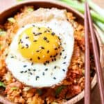 Cauliflower kimchi fried rice in a wooden bowl with wooden chopsticks and fried egg.