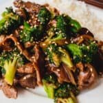 A white plate of beef and broccoli with white rice sprinkled with sesame seeds.