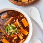 Two bowls of hot and sour soup on a white table with spoons.
