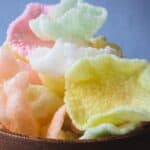 Wooden bowl with shrimp chips piled inside on top of a white table.