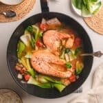 Silver ladle in a pot of salmon sinigang on a white table.
