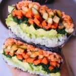 Holding spicy vegetable ongiriazu wrapped in plastic wrap with a blue plate in the back.