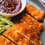 A blue plate with crispy tonkatsu and a white saucer of tonkatsu dipping sauce.