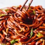 Wooden chopsticks twirling vegetarian yaki udon noodles with vegetables.