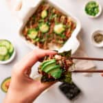 Wooden chopsticks adding salmon sushi bake to seaweed chip with avocado.