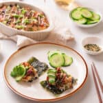 White plate with tuna sushi bake on seaweed chips with cucumber slices.
