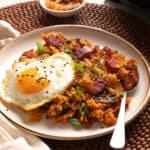Korean kimchi fried rice with an egg on a white plate and beaded placemat.